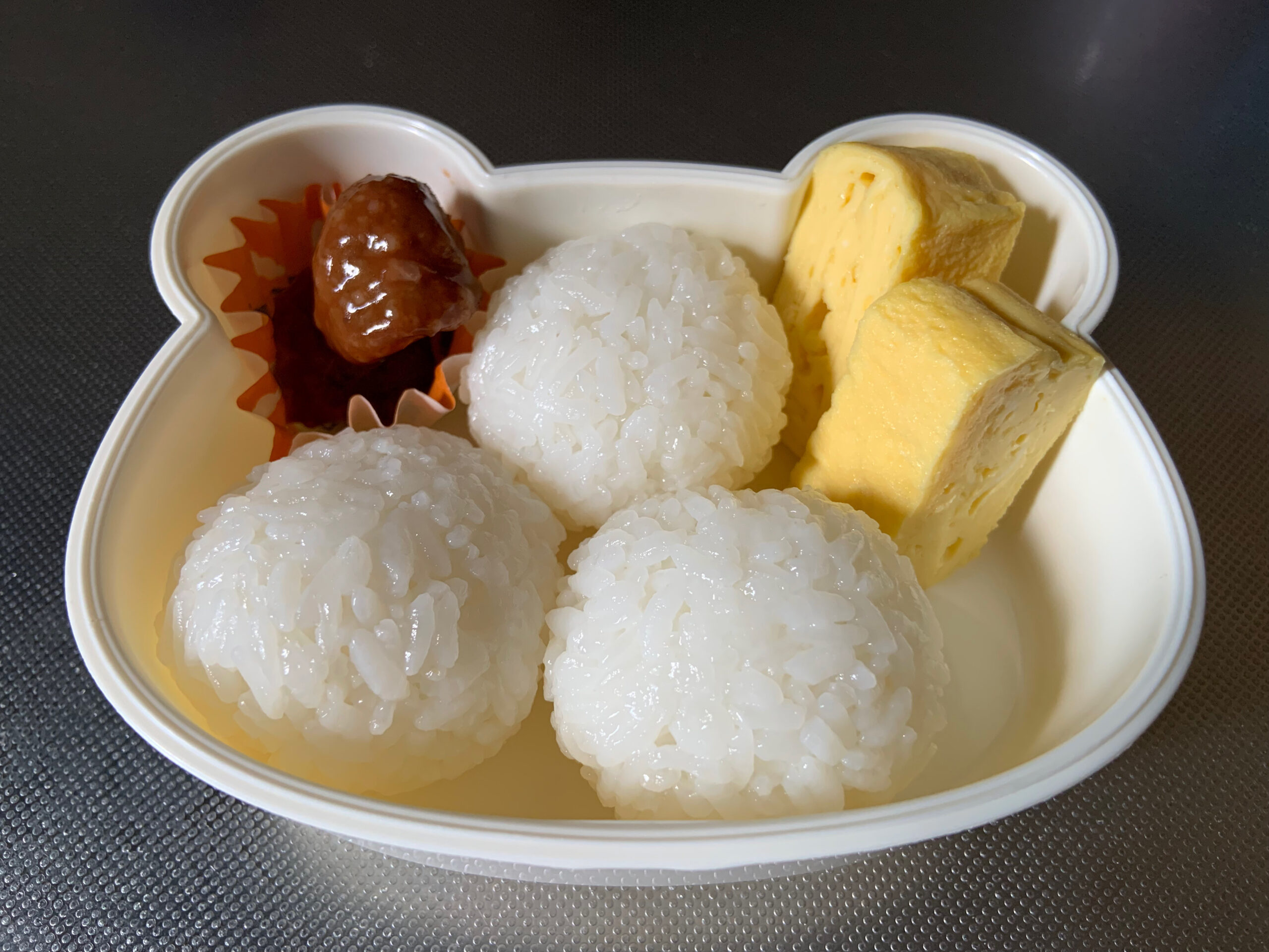子供のお弁当を作る様子。おにぎり、ミートボール、卵焼き。