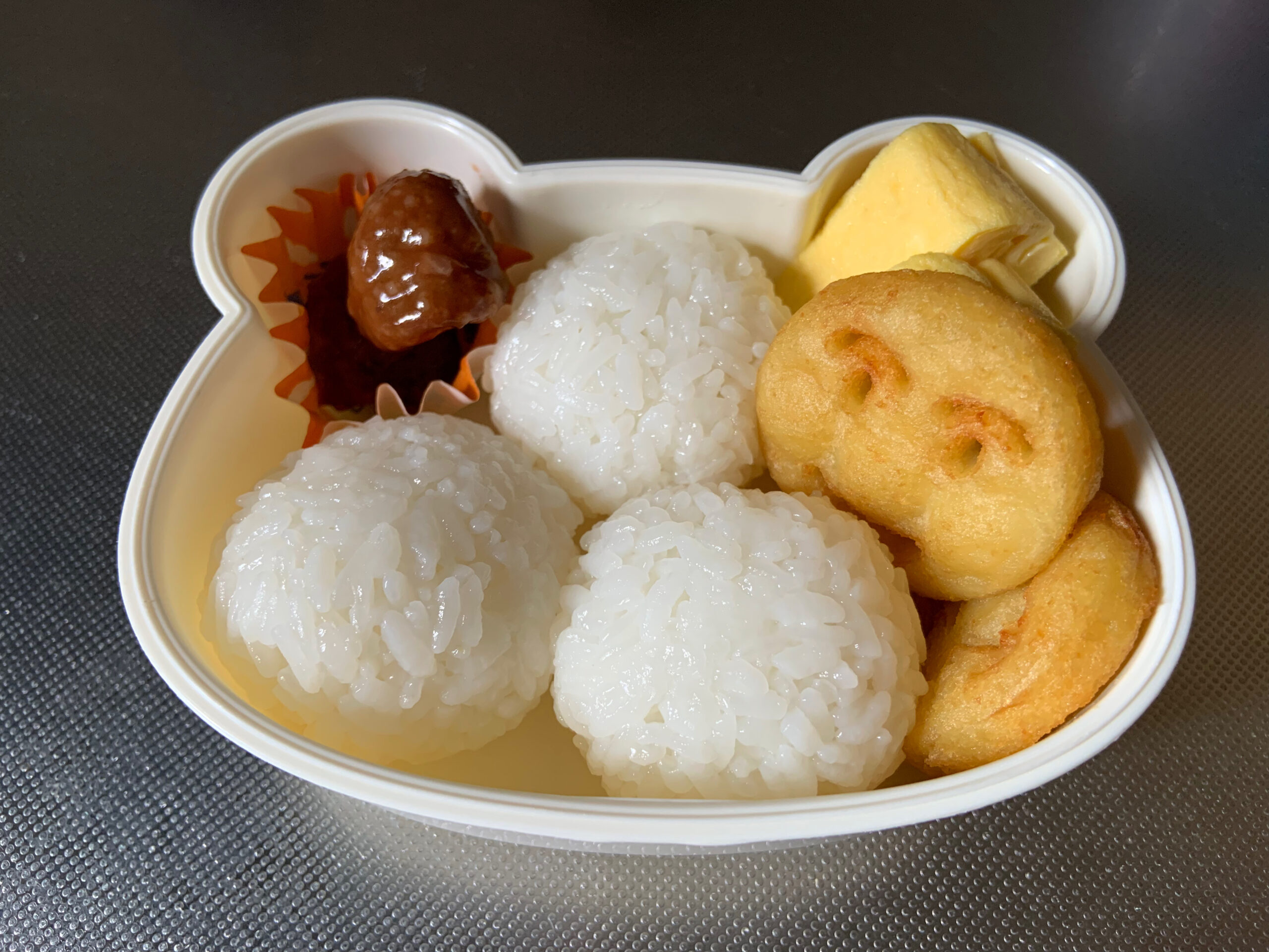 子供のお弁当を作る様子。おにぎり、ミートボール、卵焼き、アンパンマンポテト。