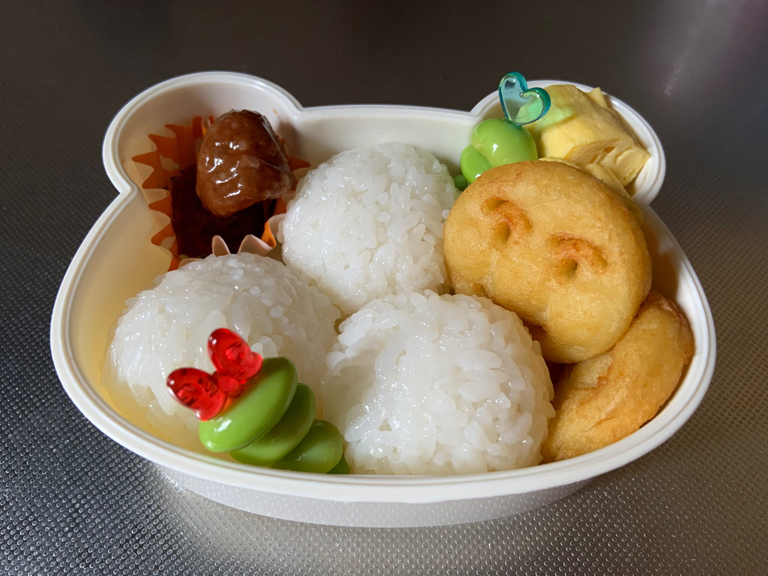 子供のお弁当を作る様子。おにぎり、ミートボール、卵焼き、アンパンマンポテト、枝豆。