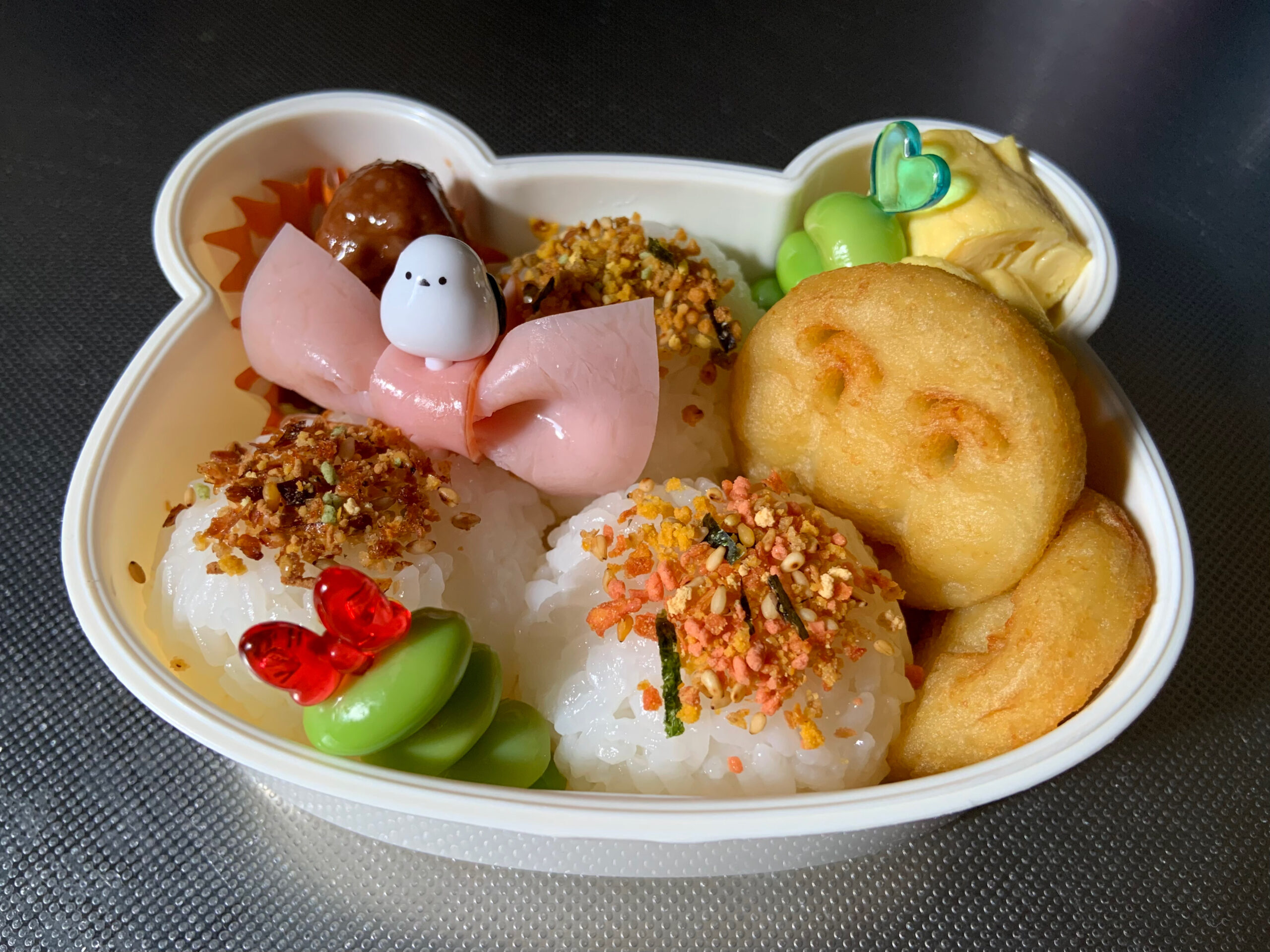 子供のお弁当を作る様子。おにぎり、ミートボール、卵焼き、アンパンマンポテト、枝豆、ハムリボン。