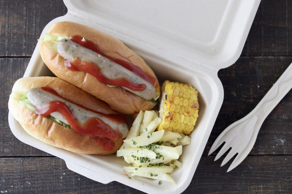 バガス弁当箱に入ったホットドッグとフライドポテトと焼きとうもろこし
